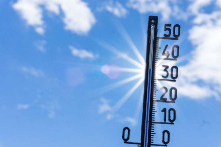 Thermometer, das knapp 40 Grad anzeigt, im Gegenlicht gegen einen blauen Himmel und strahlende Sonne fotografiert