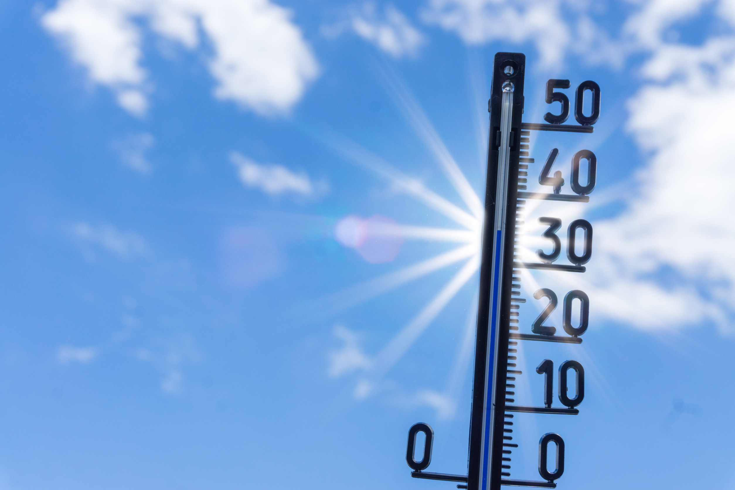 Thermometer, das knapp 40 Grad anzeigt, im Gegenlicht gegen einen blauen Himmel und strahlende Sonne fotografiert
