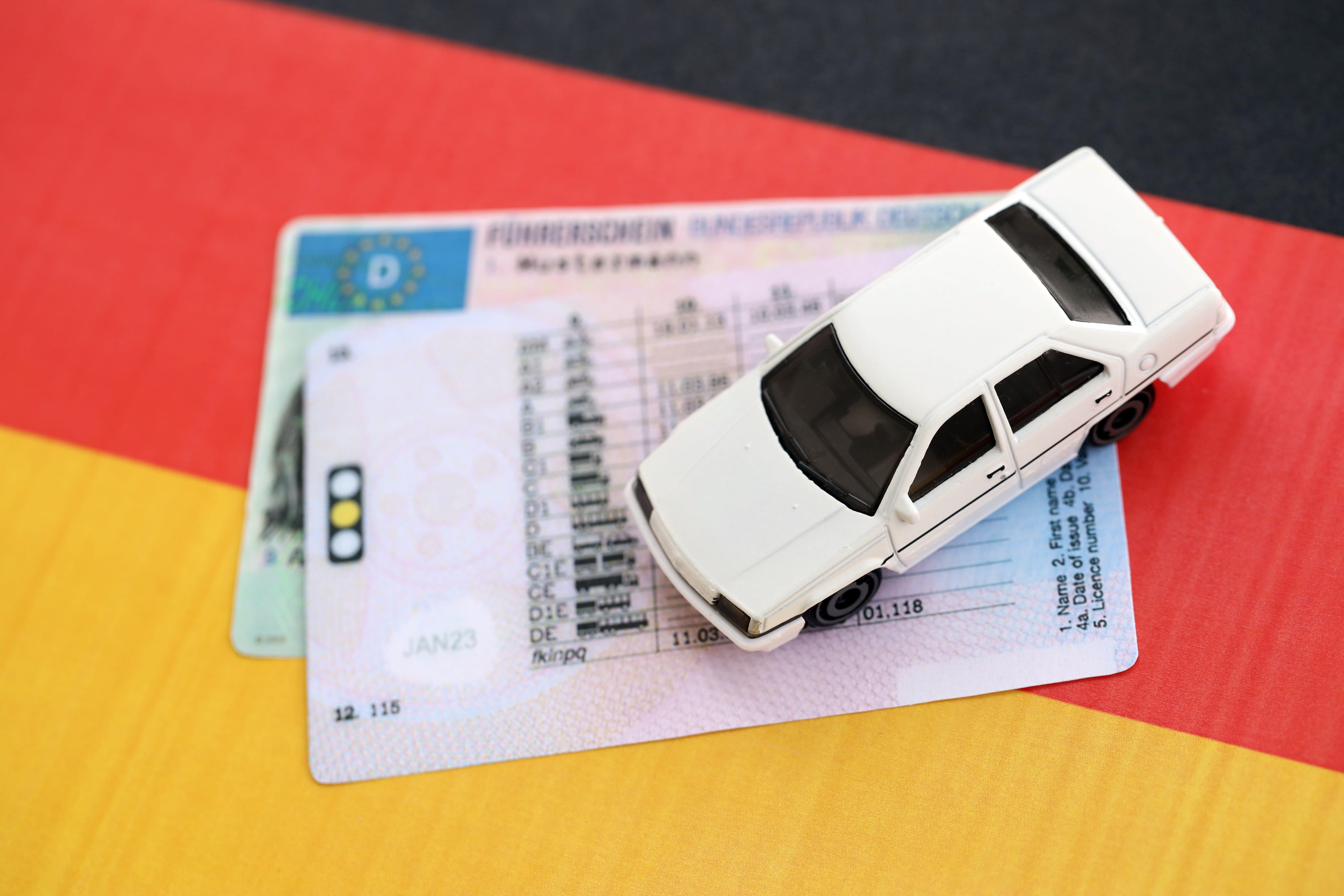 Spielzeugauto und deutscher Führerschein auf deutscher Flagge