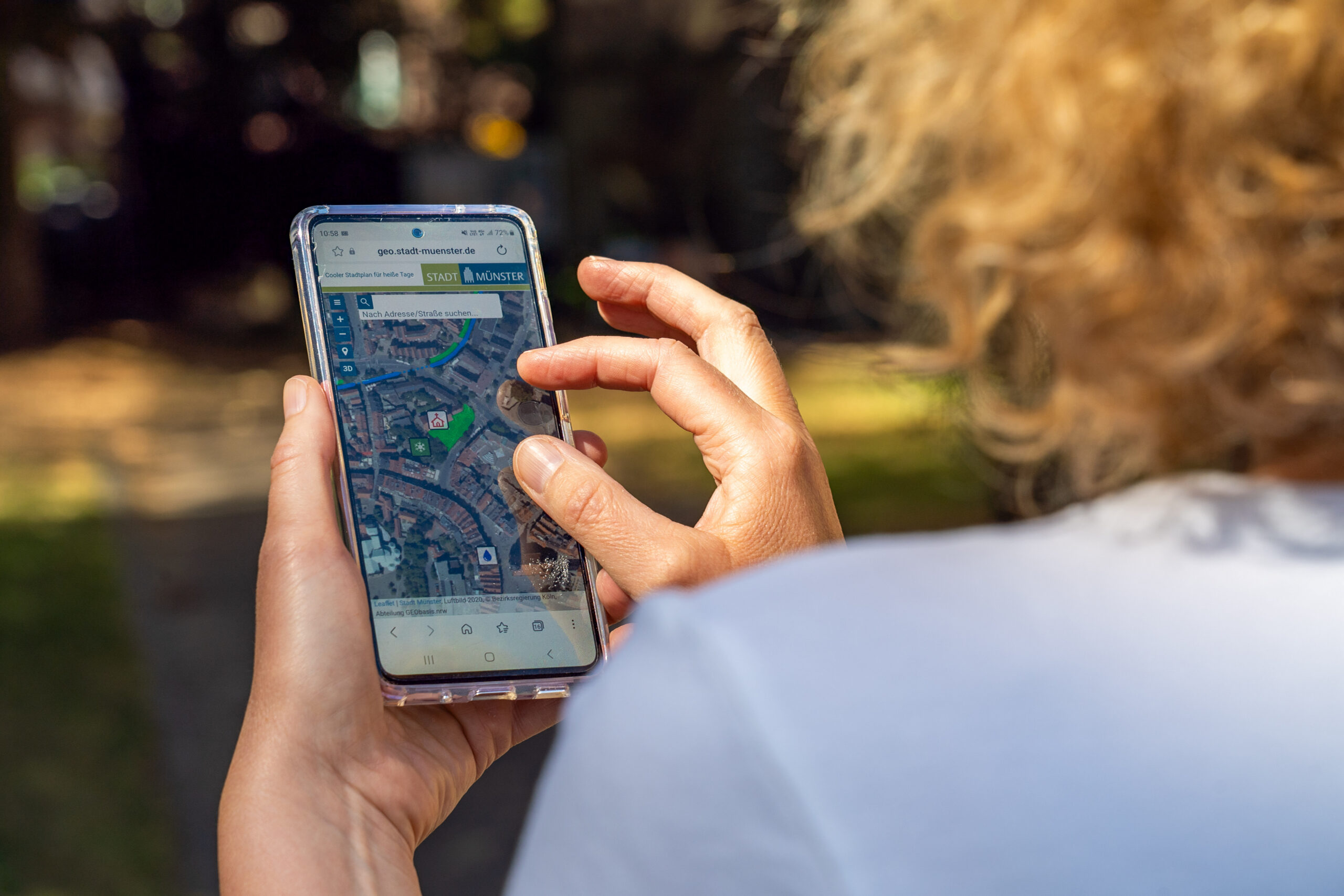 Blick über die Schulter einer Frau, die auf ihrem Smartphone die Coole Karte der Stadt Münster geöffnet hat