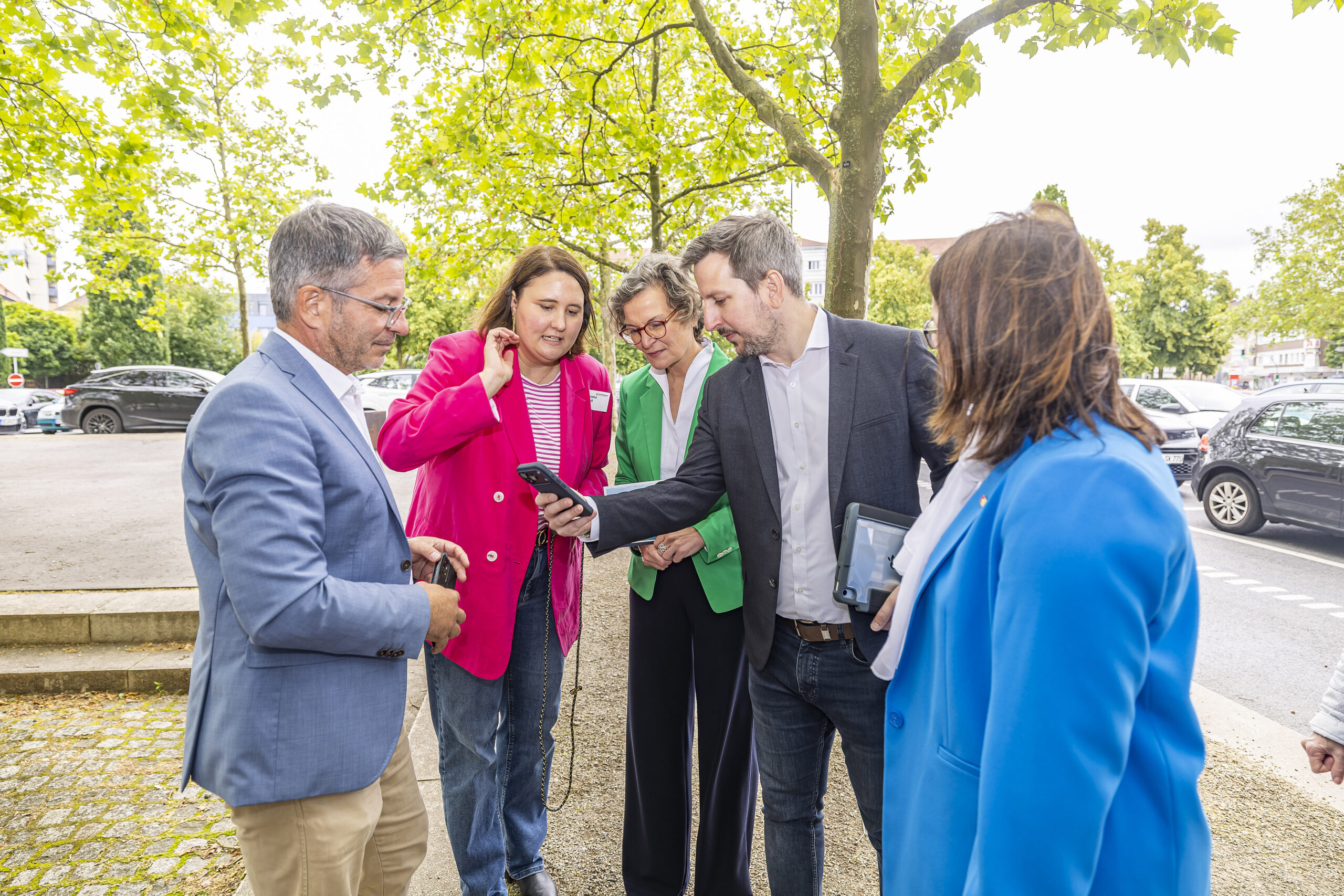 Mehrere Personen auf einem Gehweg, schauen auf ein Smartphone