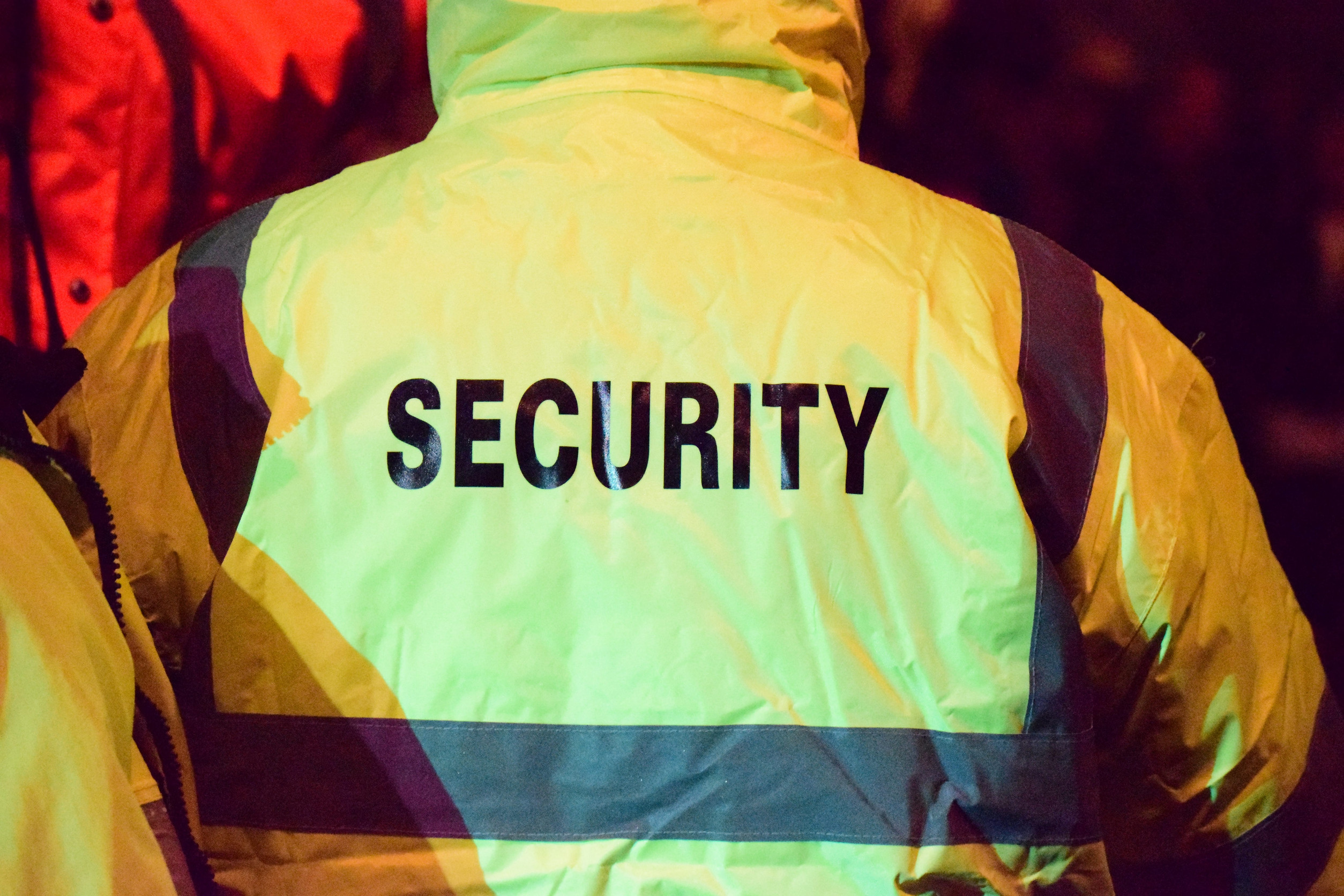 Person mit neongelbem Regenzeug von hinten, auf dem Rücken steht in schwarzer Schrift: Security