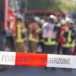 Absperrband Feuerwehr dahinter verschwommen Feuerwehrfahrzeuge und Feuerwehreinsatzkräfte