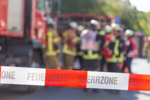 Absperrband Feuerwehr dahinter verschwommen Feuerwehrfahrzeuge und Feuerwehreinsatzkräfte