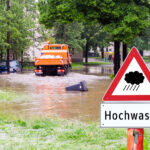 Geflutete Straße in Deutschland, Schild Hochwasser im Vordergrund