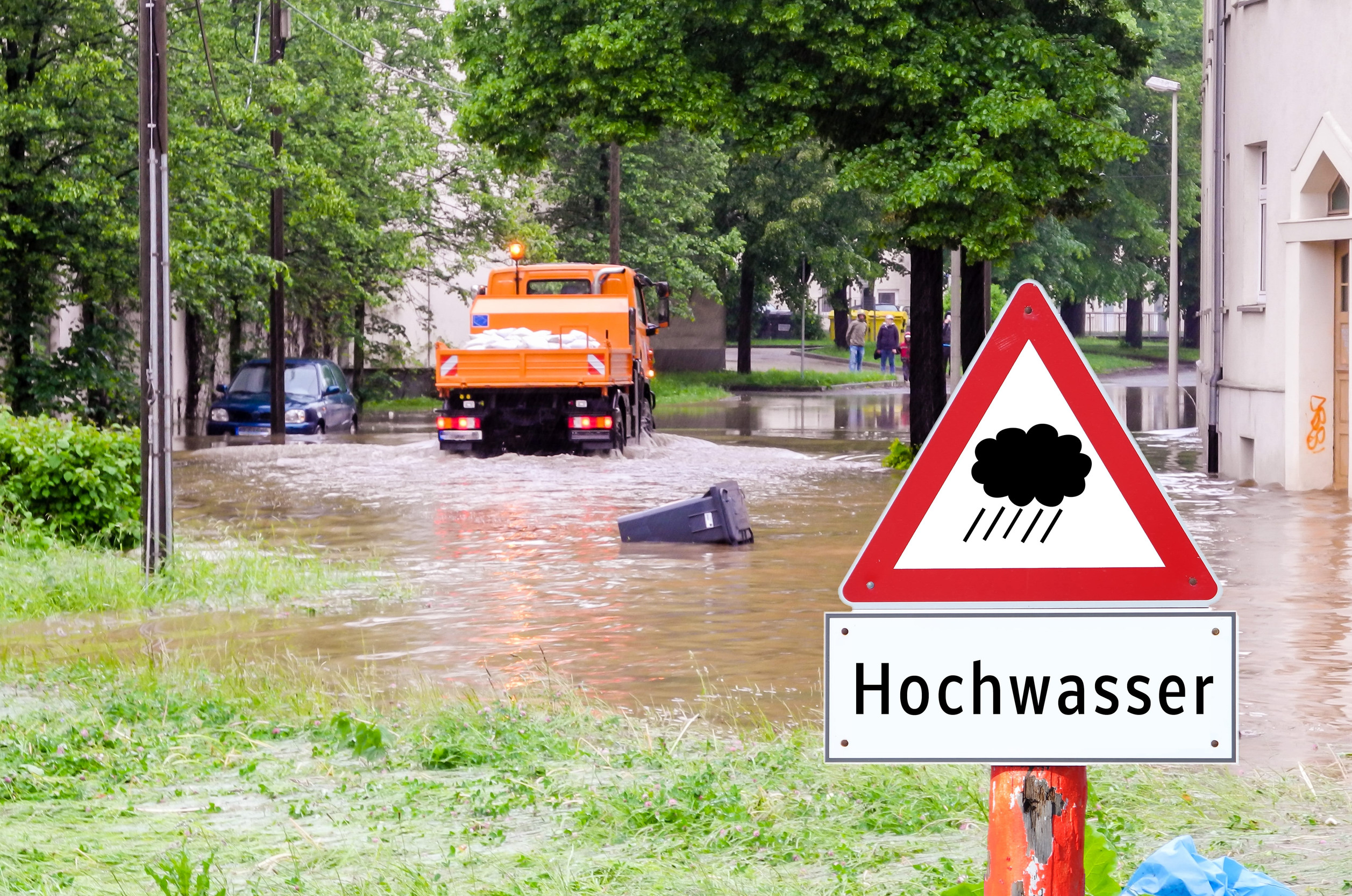 Geflutete Straße in Deutschland, Schild Hochwasser im Vordergrund