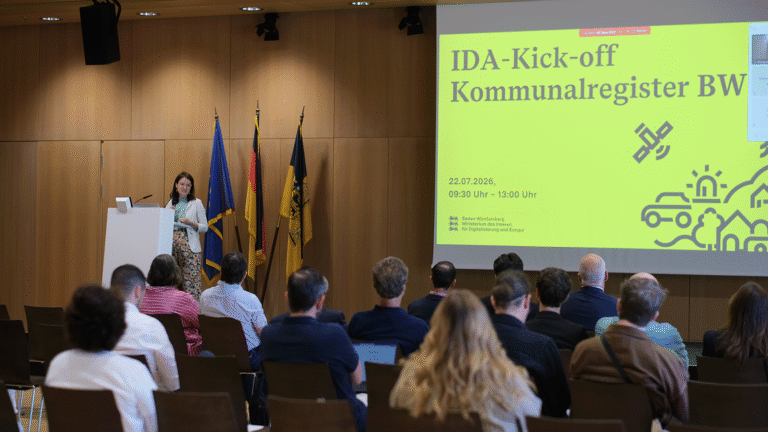 Abgedunkelter Saal mit Holzvertäfelung, Blick über Zushcauerköpfe aufs Podium, wo man eine grüße Projektion und verschiedene Flaggen sieht.