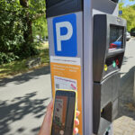 Parkscheinautomat, davor Arm und Hand mit Handy