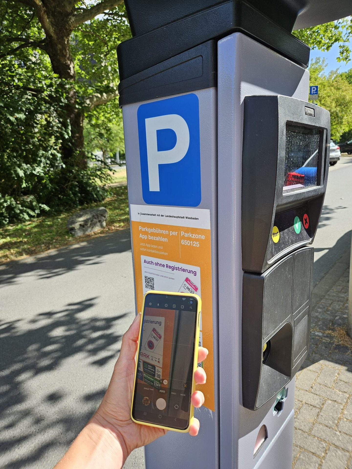 Parkscheinautomat, davor Arm und Hand mit Handy