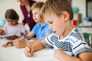 Junge Grundschüler mit Lehrer bei Schreibübungen
