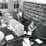 Körniges Schwarz-Weiß-Foto, Großraum-Büro mit vielen Arbeitsplätzen und Ordnern und Drehregister