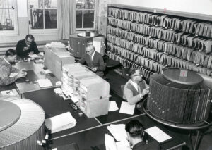 Körniges Schwarz-Weiß-Foto, Großraum-Büro mit vielen Arbeitsplätzen und Ordnern und Drehregister