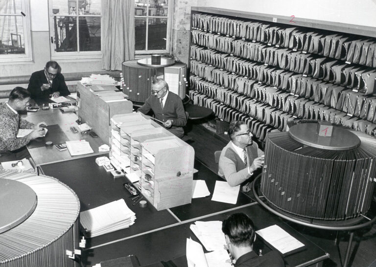Körniges Schwarz-Weiß-Foto, Großraum-Büro mit vielen Arbeitsplätzen und Ordnern und Drehregister