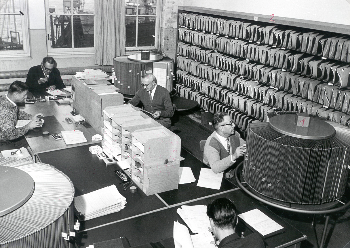 Körniges Schwarz-Weiß-Foto, Großraum-Büro mit vielen Arbeitsplätzen und Ordnern und Drehregister