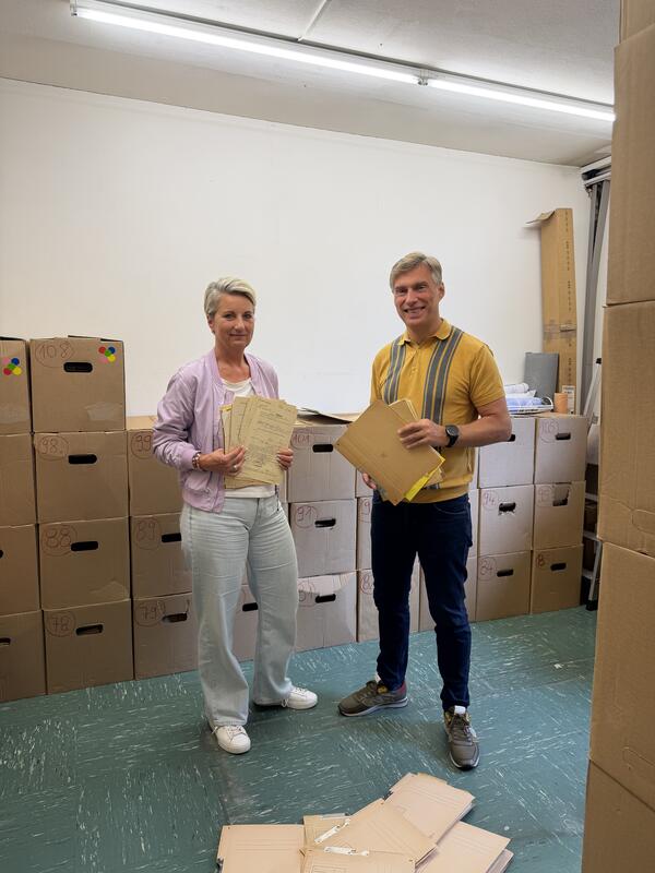 zwei Personen stehen vor Kartons voller Akten