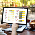 Person am Laptop, am Bildschirm ein Mock-Up-Umfrageformular, sonniger Schreibtisch mit Muffins