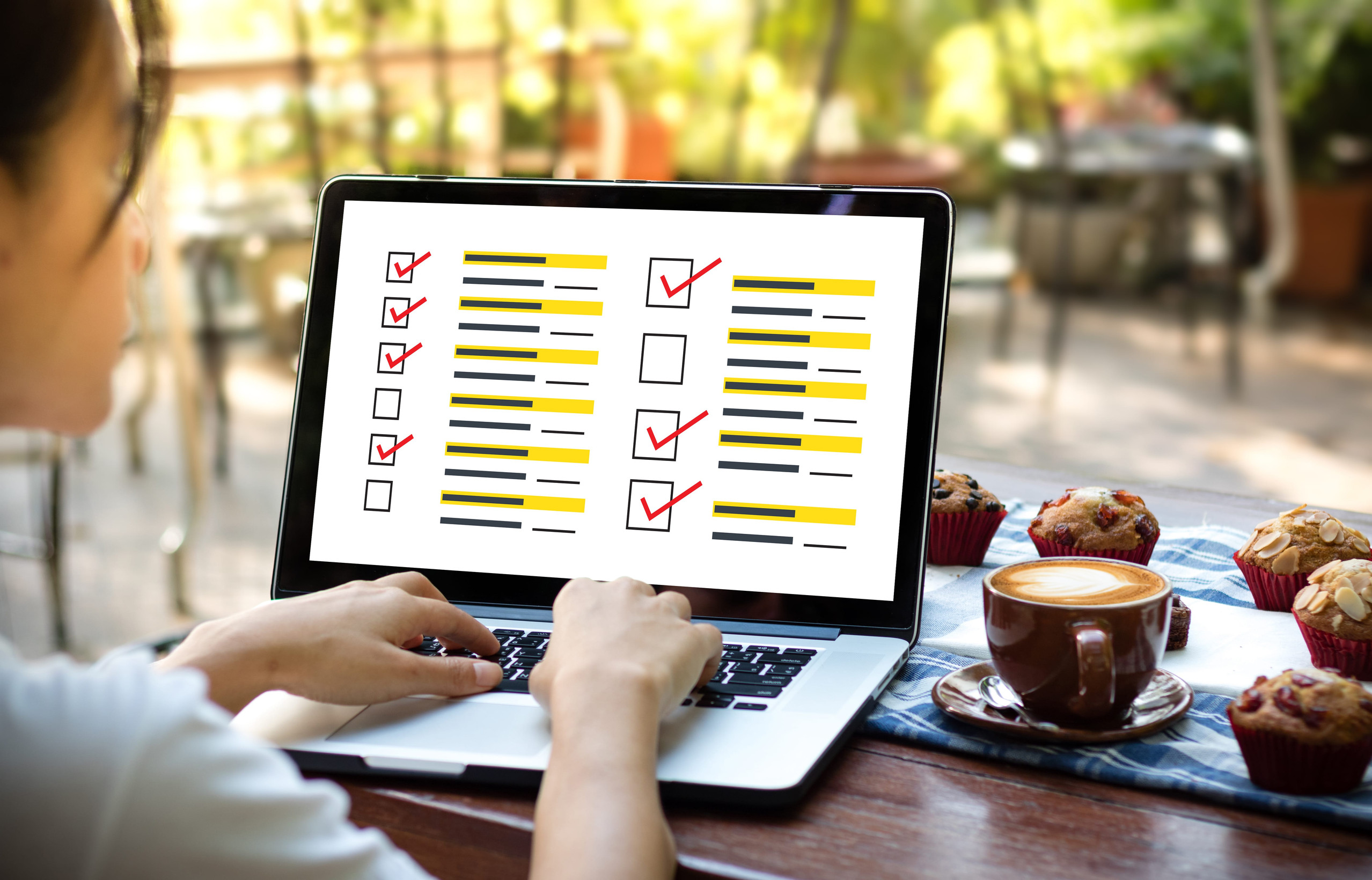 Person am Laptop, am Bildschirm ein Mock-Up-Umfrageformular, sonniger Schreibtisch mit Muffins