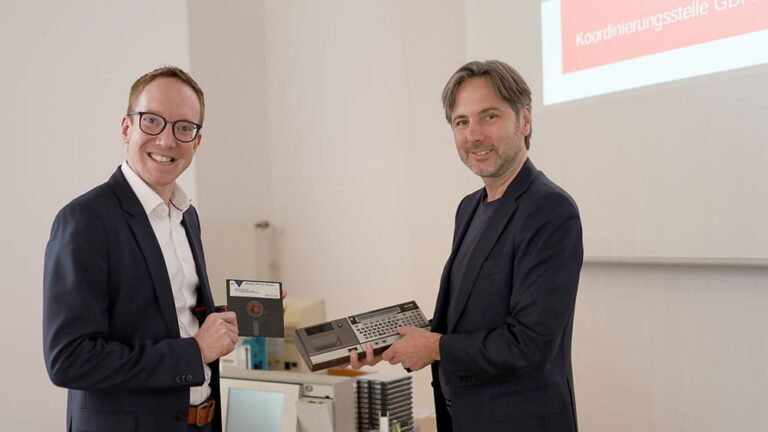 Zwei Personen halten eine 5¼-Diskette zur Datensicherung in die kamera
