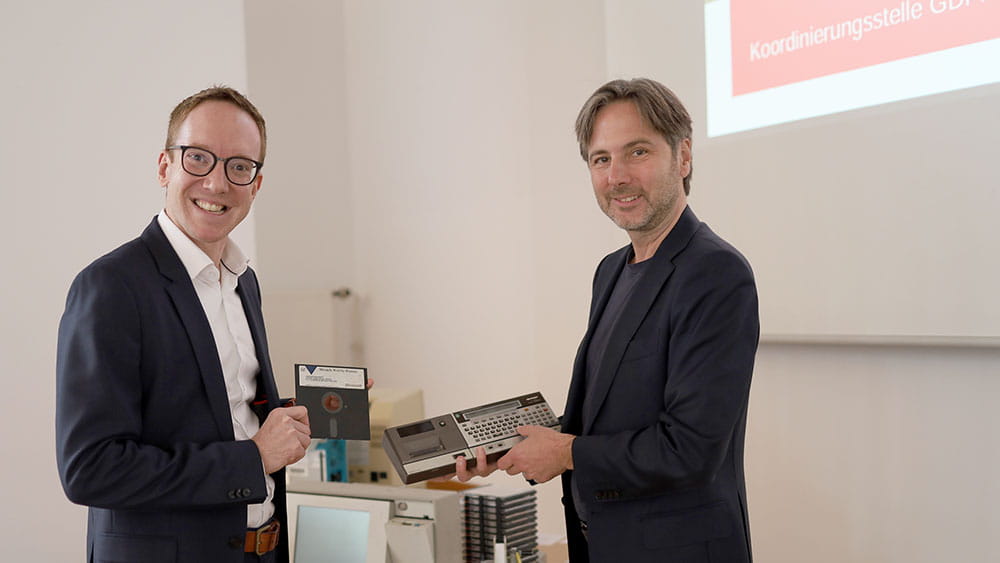 Zwei Personen halten eine 5¼-Diskette zur Datensicherung in die kamera