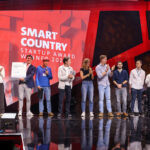 Personengruppe auf einer rot ausgestalteten Bühne mit Aufschrift "Smart Country Startup Award"