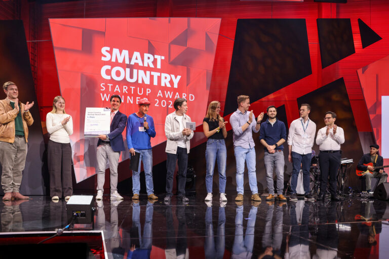 Personengruppe auf einer rot ausgestalteten Bühne mit Aufschrift "Smart Country Startup Award"