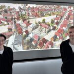 Zwei Personen vor einem Monitor auf dem historische 3D-Modell Gütersloh um 1900 zu sehen ist