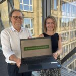 Mann und Frau halten der Kamera ein Laptop entgegen, darauf Formular