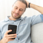 Entspannter junger Mann mit Handy auf einem hellen Sofa.