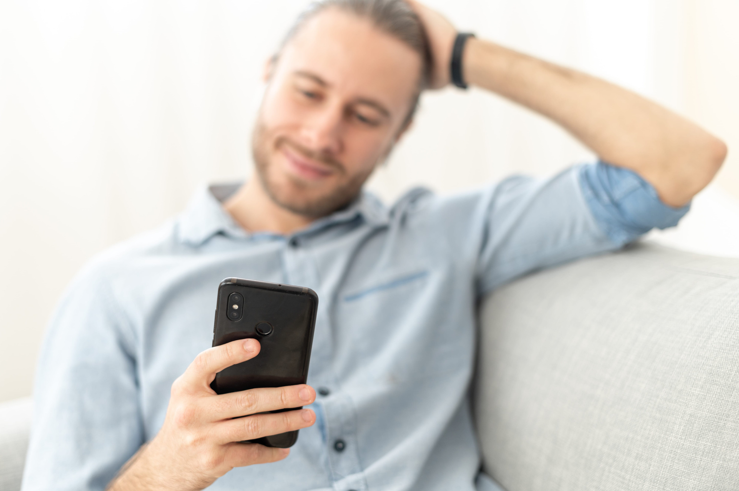 Entspannter junger Mann mit Handy auf einem hellen Sofa.