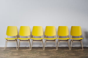 Sechs leere gelbe Stühle stehen in einer Reihe vor einer weißen Wand