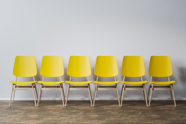 Sechs leere gelbe Stühle stehen in einer Reihe vor einer weißen Wand
