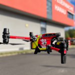 Drohne in der Luft, im Hintergrund ist verschwommen ein Gebäude der Feuerwehr Hanau zu sehen
