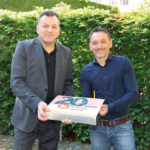 Zwei Männer halten eine Torte mit der Aufschrift "20 Jahre komxwork"