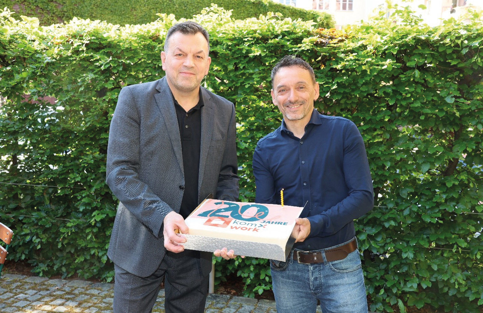 Zwei Männer halten eine Torte mit der Aufschrift "20 Jahre komxwork"