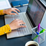 Blick auf Schreibtisch: Laptop, Hände, gefüllte Kaffeetasse