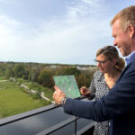 Ein Mann und eine Frau blicken mit einem Tablet in der Hand auf einen Park, dessen digitale Version auf dem Tablet zu sehen ist
