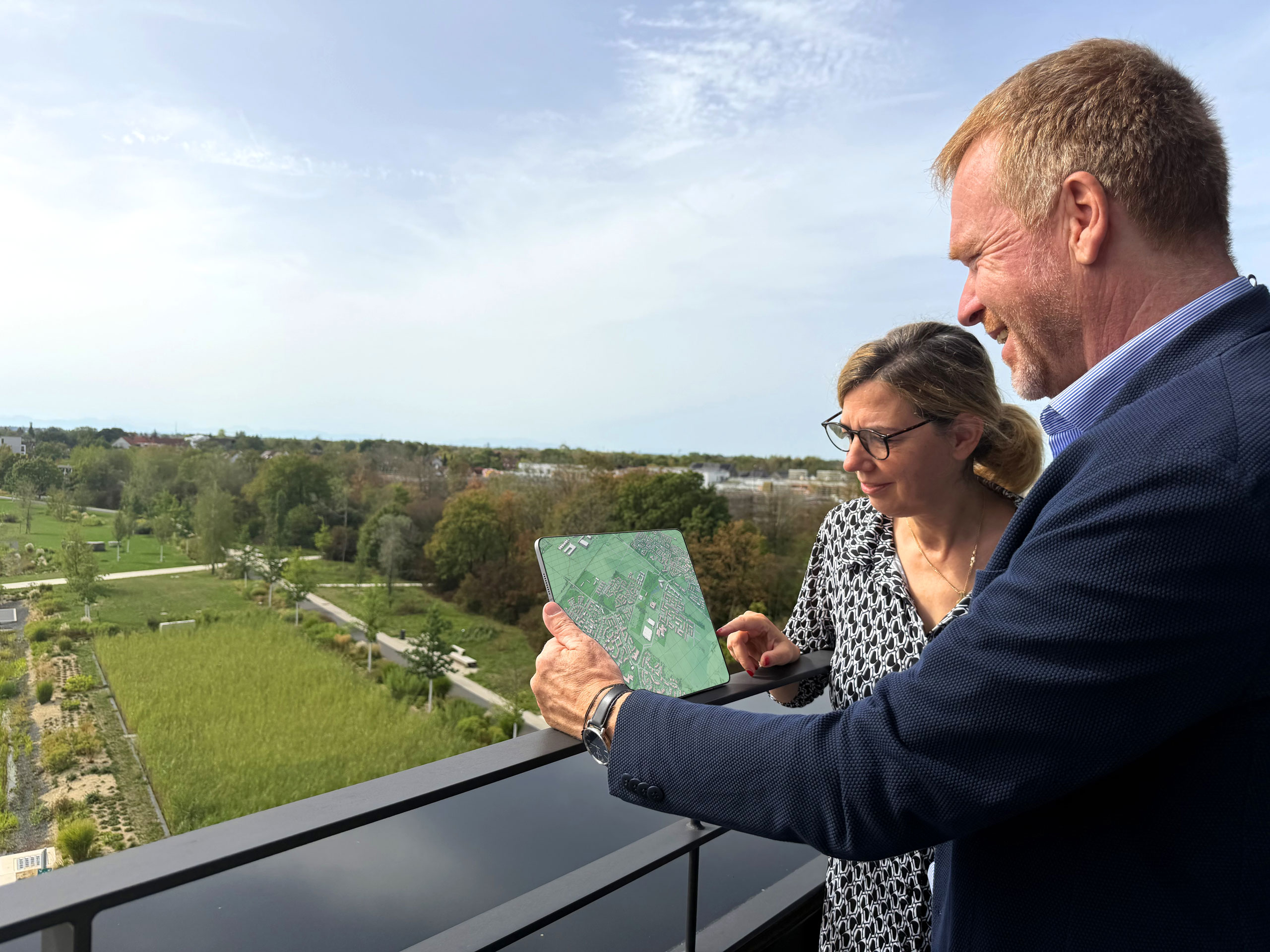 Ein Mann und eine Frau blicken mit einem Tablet in der Hand auf einen Park, dessen digitale Version auf dem Tablet zu sehen ist