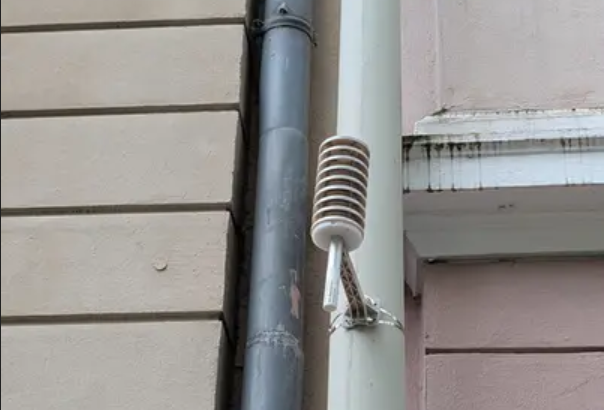 Hausfassade mit Klimasensor, dieser sieht etwa aus wie ein weiß angestrichenes Mikrofon.