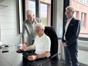 Christoph Schnaudigel, Landrat Kreis Karlsruhe sitzt vor einem Rechner, ihm schauen über Schulter ein Dezernat des LRA Karlsruhe und regisafe Geschäftsführer Frank Schellmann