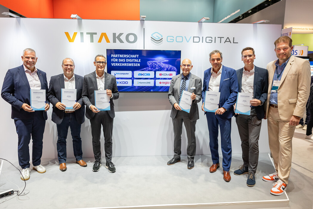 Eine Reihe von Personen an einem Messestand, auf einem Monitor steht Partnerschaft für das digitale Verkehrswesen