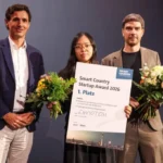 Drei Personen mit Urkunde und Blumenstrauß