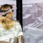Frau mit VR-Brille schaut durch ein Panoramafenster auf eine Stadtlandschaft
